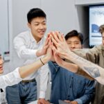 A group of young professionals high-fiving during a collaborative office meeting symbolizing teamwork and unity.