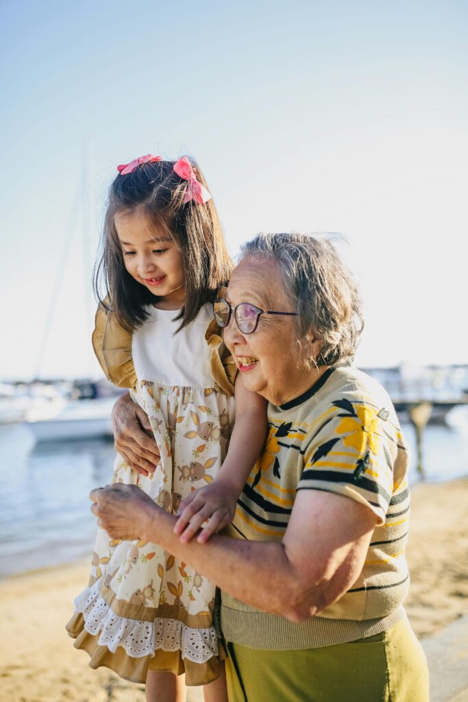 Home Happy Asian grandmother and granddaughter enjoying a sunny day at the beach, capturing joyful family moments.